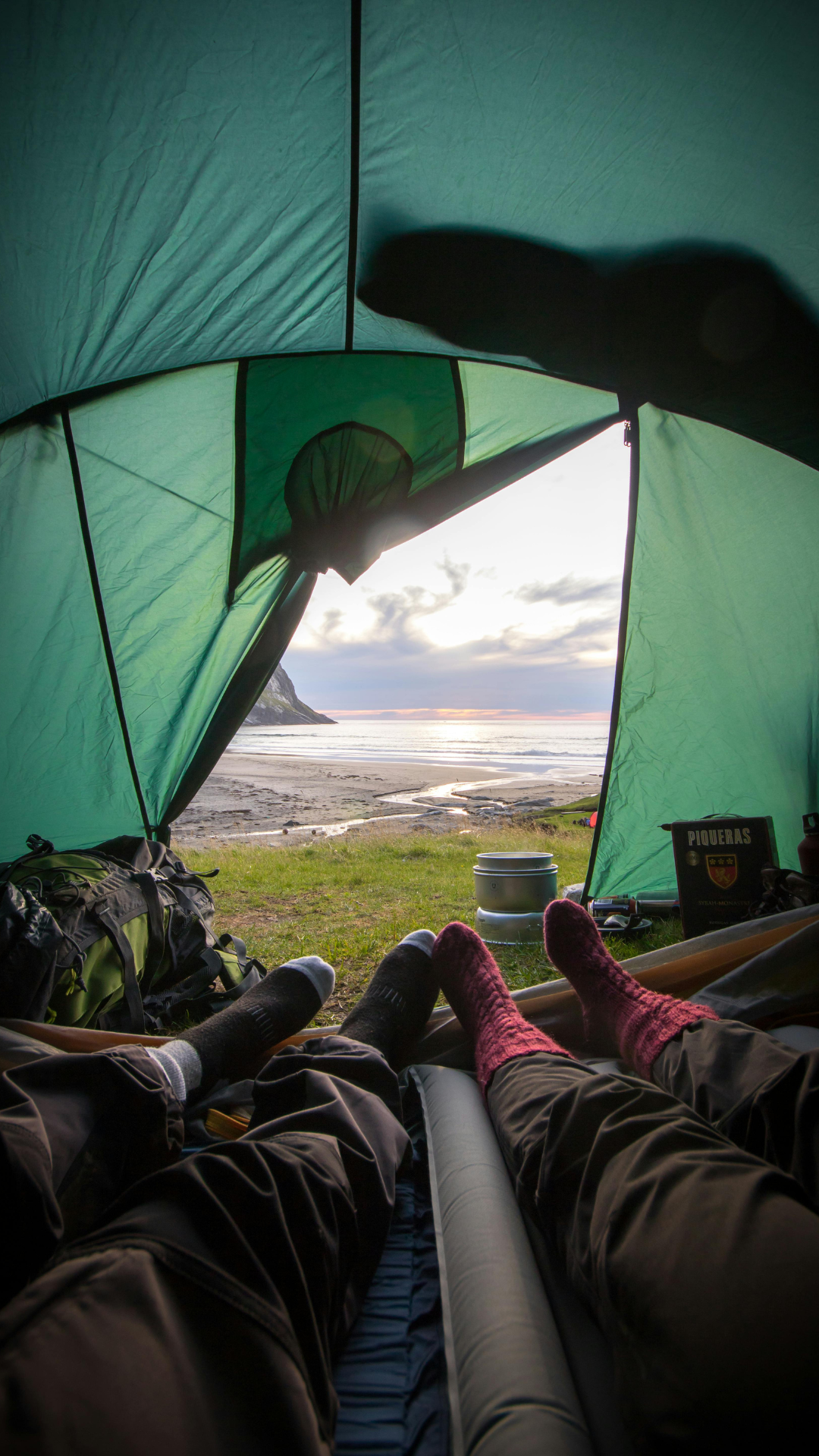 Two friends camping on the beach in a small green tent